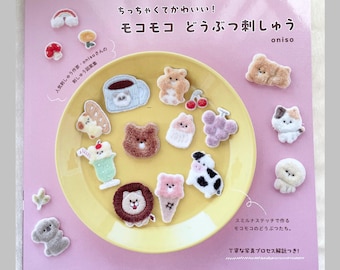 May include: A pink craft book titled "ちっちゃくてかわいい！モコモコ どうぶつ刺しゅう" featuring a yellow plate filled with various small, fuzzy animal and food-themed embroidered patches, including a lion, cow, bear, and ice cream cone, with additional patches scattered around the cover.