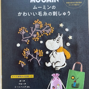 May include: A book cover with a white Moomin character on a dark blue background. The title is "Moomin's Cute Yarn Embroidery". The book cover also features a small pink bag with a Moomin character and a green bag with a house and trees.