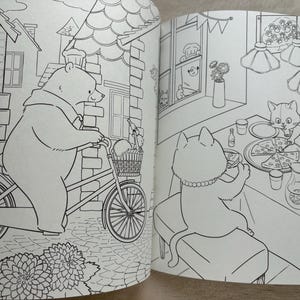 May include: Black and white illustration from a children's coloring book. A bear rides a bicycle with a basket, while cats enjoy pizza at a table. The scene is set in a town with buildings and flowers.