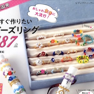 Könnte beinhalten: Ein Buch mit einem rosa Einband, das eine Sammlung von 187 Perlenringen in verschiedenen Farben und Designs zeigt. Der Buchtitel lautet "Bead Rings 187" und der Text "Jetzt kannst du es machen!" ist in Japanisch geschrieben.