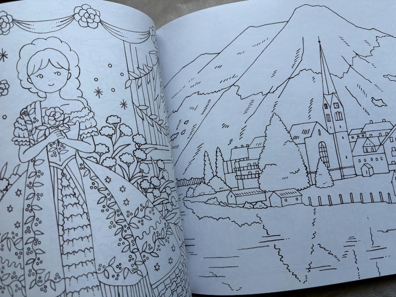 May include: A coloring book open to two pages. One page features a detailed illustration of a woman in a dress holding flowers. The other page shows a landscape with mountains, a church, and a lake, all in black and white line art.