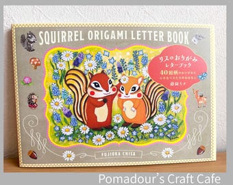 May include: A rectangular Squirrel Origami Letter Book with a gray cover featuring two illustrated squirrels surrounded by white daisies and blue flowers. The text reads SQUIRREL ORIGAMI LETTER BOOK, FUJIOKA CHISA, and Japanese characters in a red circle.
