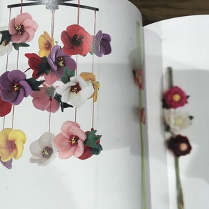 May include: A colorful felt flower mobile with red, pink, white, yellow, and purple flowers hanging from a black metal frame.