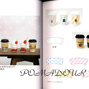 May include: A collection of miniature coffee cups and desserts, including a parfait with strawberries and whipped cream, a coffee cup with a brown and white striped design, and a coffee cup with a yellow and white striped design. The text "POMADOUR" is visible in the image.