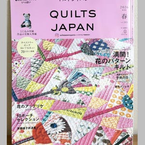 Puede incluir: Una portada de revista Quilt Japan rosa y blanca con texto japonés. La portada presenta un diseño de colcha de patchwork con piezas de tela rosa, amarilla y azul. El texto incluye "QUILTS JAPAN" y "2026 Primavera".