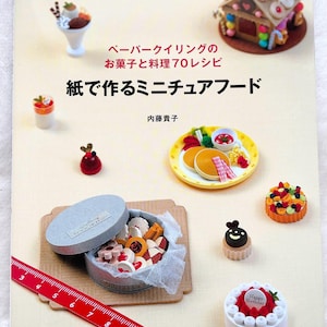 Könnte beinhalten: Buchcover mit Miniatur-Papier-Essen, darunter Desserts und ein Pfannkuchen-Frühstück. Der Titel lautet "Miniatur-Essen aus Papier" auf Japanisch. Ein rotes Lineal liegt in der Nähe einer Dose mit Papierkeksen.