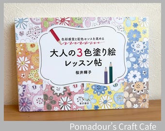 May include: A rectangular book with a white central label featuring the Japanese text "大人の3色塗り絵レッスン帖" and "色彩感覚と配色センスを高める". The cover is decorated with a grid of colorful, hand-drawn floral patterns in shades of pink, yellow, blue, and brown, accented by illustrations of three colored pencils.