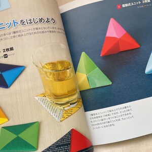 May include: A book open to a page showing instructions for origami. The page shows a diagram of a folded origami triangle with the text "部式ユニット" in Japanese. The page also shows a glass of tea and a folded origami coaster.