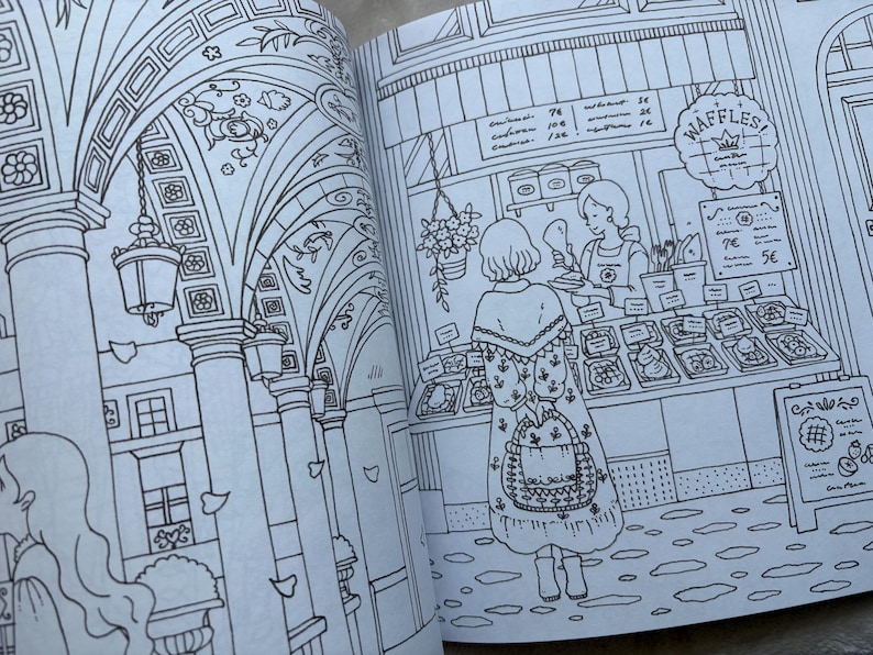 May include: A detailed black and white illustration from a coloring book. The image depicts a European street scene with a waffle shop and a woman in a patterned dress. The shop has a sign that says "Waffles!" and a menu board.