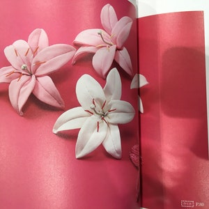 May include: Three fabric lily flowers on a pink background. Two are pink and one is white.