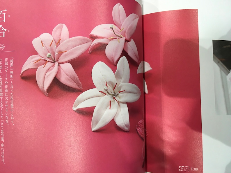 May include: Three fabric lily flowers on a pink background. Two are pink and one is white.