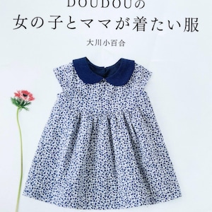 Puede incluir: Una portada de libro con fondo blanco y un vestido floral azul y blanco sobre una superficie blanca. El título del libro es "DOUDOU's Girls and Moms Want to Wear Clothes" en japonés. La portada del libro también incluye el texto "Pomadour's" en rosa.