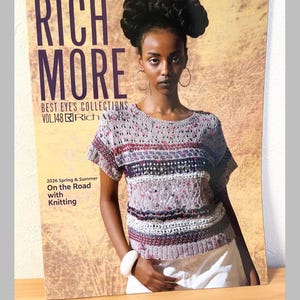 May include: A woman wearing a short-sleeved, patterned knit top, posing with a magazine titled "RICH MORE." The magazine cover features the text "BEST EYE'S COLLECTIONS" and "2026 Spring & Summer On the Road with Knitting."