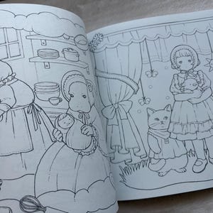 May include: Open book with black and white illustrations of a coloring book. One page shows a woman cooking with a cat, and another page shows a girl holding a doll with two cats. The illustrations have a vintage, storybook style.