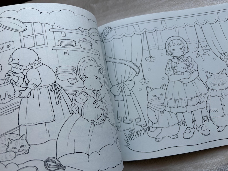 May include: Open book with black and white illustrations of a coloring book. One page shows a woman cooking with a cat, and another page shows a girl holding a doll with two cats. The illustrations have a vintage, storybook style.