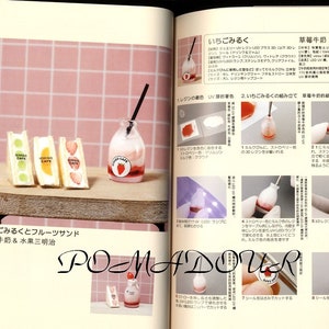 May include: A close-up of a miniature strawberry milk bottle and three miniature fruit sandwiches. The sandwiches are filled with fruit and have a pink, white, and green color scheme. The bottle is pink and white with a red strawberry on the front. The text "HONJIGO CAFE" is printed on the sandwiches.