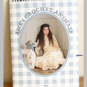 May include: A book titled "Ame's Crochet Animals" with a light blue and white checkered pattern background. The cover features a woman in a cream-colored dress and a small crochet animal. The text "Pomadour's Craft" is at the bottom.