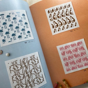 May include: A book with four different cross-stitch patterns. The patterns are on white fabric and feature different designs, including mushrooms, animals, and geometric shapes. The book has page numbers 41, 43, and 44.