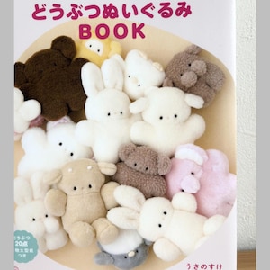 May include: A craft book titled "ふわふわ もふもふ 手ぬいで作る どうぶつぬいぐるみ BOOK" featuring a collection of small, plush animal figures in various colours including white, brown, tan, and pink. The cover displays multiple soft, fuzzy stuffed animals.