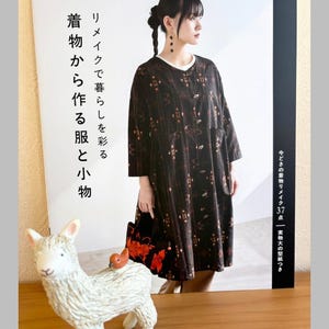 以下が含まれることがあります： 着物柄のドレスを着た女性が表紙の書籍。書籍の前には、背中に小さな鳥を乗せた白いセラミック製のラマの置物があります。書籍のタイトルは「着物から作る服と小物」です。