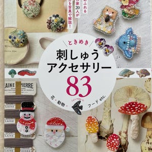 Puede incluir: Una portada de libro con el título "刺しゅうアクセサリー 83" (que significa "Accesorios bordados 83") e imágenes de varios accesorios bordados, incluyendo flores, setas, un muñeco de nieve y un Papá Noel.