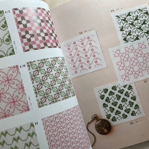 May include: A book with pages showing different embroidery patterns. The patterns are in shades of green, pink, and brown. The numbers 07, 09, 11, 13, 14, 15, and 16 are visible on the pages.