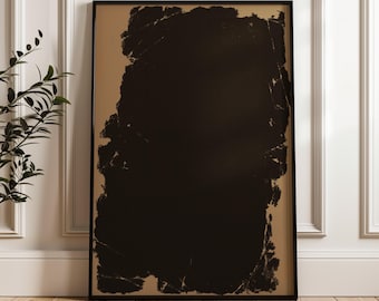 May include: A framed abstract art print featuring a large, textured black shape against a tan background. The artwork is enclosed in a black frame and leans against a white wall and wooden floor.