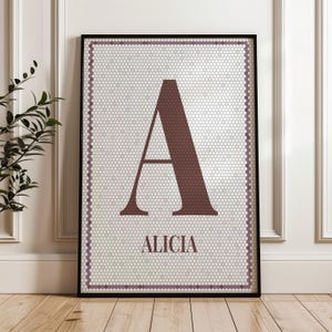 May include: A framed print displaying a burgundy letter "A" on a white honeycomb patterned background. The name "Alicia" is printed below. The artwork is enclosed in a black frame, suitable for home decor.