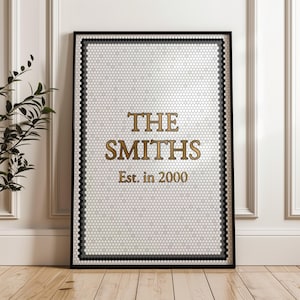 May include: A framed artwork with a white honeycomb design and black and grey borders. The text "THE SMITHS" is in gold lettering, with "Est. in 2000" below. The artwork is in a black frame and is leaning against a white wall.