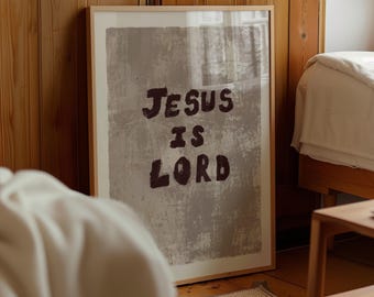 May include: A framed print with the words "JESUS IS LORD" in dark brown lettering. The background is a textured gray, and the frame is a light wood color. The print is displayed in a room with wooden paneling and a bed.