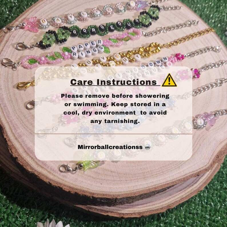 May include: A collection of colourful beaded bracelets with letter beads spelling out words like "Gorgeous", "Paper Rings", and "Love You". The bracelets are displayed on a wooden surface with a care instructions card that reads "Please remove before showering or swimming. Keep stored in a cool, dry environment to avoid any tarnishing. Mirrorballcreationss".