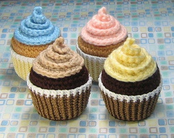 May include: Three crocheted cupcakes, one blue, one pink, and one yellow, with chocolate frosting and white sprinkles.