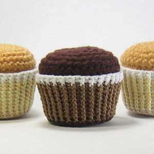 May include: Three crocheted cupcakes, one yellow, one brown, and one yellow with white frosting.