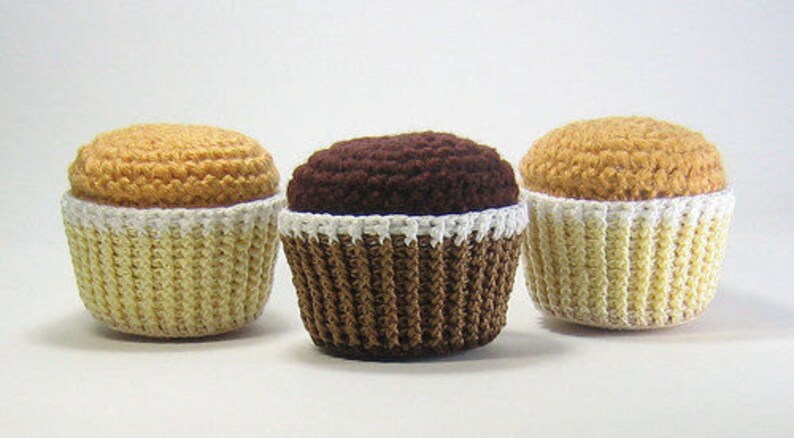 May include: Three crocheted cupcakes, one yellow, one brown, and one yellow with white frosting.