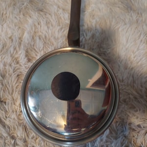 May include: A silver saucepan with a wooden handle. The saucepan has a black circle in the center of the lid.