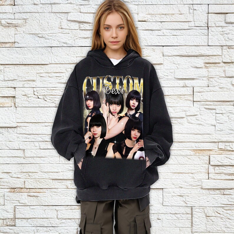 Pu&ograve; includere: Felpa con cappuccio nera con una grafica di un gruppo di donne con la scritta "Custom Text" in lettere dorate. La felpa ha un cappuccio con coulisse e una tasca frontale. La modella indossa la felpa.