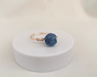 May include: A gold wire ring with a blue, textured, round bead.