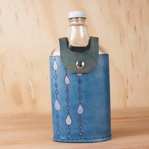 May include: A blue leather bottle holder with a glass bottle inside. The bottle holder has a design of white teardrop shapes and blue circles.