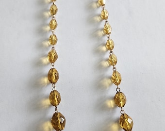 May include: A gold tone necklace with a chain and amber colored faceted glass beads.