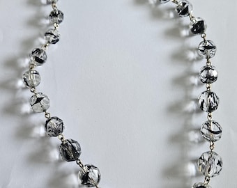 May include: A silver chain necklace with clear faceted glass beads with black markings.