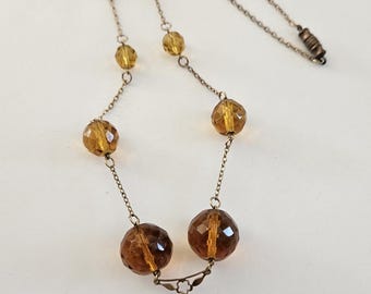 May include: A gold chain necklace with a brown faceted glass pendant and smaller brown faceted glass beads.