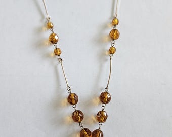 May include: A silver necklace with a long, dangling drop featuring amber-colored glass beads.