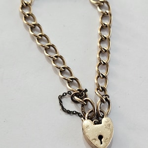 May include: A gold-colored bracelet with a heart-shaped padlock clasp. The bracelet features a chain link design. The padlock has a keyhole and is attached to the chain with a small chain.