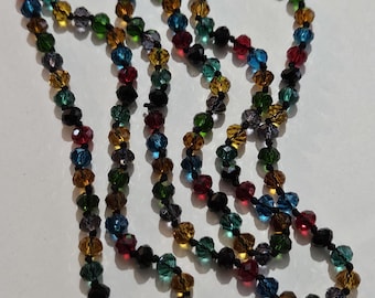 May include: A multi-colored beaded necklace. The necklace features a variety of jewel-toned beads, including red, blue, green, and yellow, strung together on a black cord. The beads are faceted, catching the light and creating a sparkling effect.