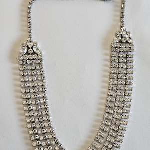 Può includere: Una collana argentata con più file di piccole e scintillanti strass. La collana presenta una delicata catena e una chiusura a fermaglio. Il design include una serie di file graduate di strass, creando un effetto a cascata. Questo elegante pezzo è adatto alle occasioni formali.