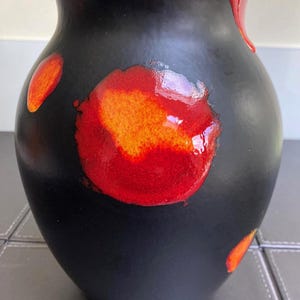 May include: A black ceramic vase with vibrant red and orange abstract designs. The vase has a rounded body and a slightly flared rim. The red and orange accents create a striking contrast against the dark background, making it a decorative piece.