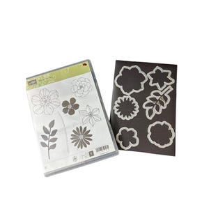 May include: A clear plastic stamp set featuring floral and leaf outlines alongside a black magnetic sheet containing six silver metal cutting dies that correspond to the shapes of the flowers and leaves printed on the stamp set packaging.