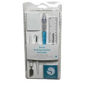 May include: A white plastic package containing a Silhouette tool kit. The kit includes a ruler, a scraper, a hook, a weeding tool, a pick-me-up tool, and a small blue square with the Silhouette logo. The package is labeled "Tool kit, Kit de herramientas, Kit d'outils".
