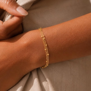 May include: A delicate gold bracelet featuring a fine chain design with small, evenly spaced spherical beads along the length. The bracelet has a polished metallic finish and rests against the skin, showcasing a simple and refined link structure.