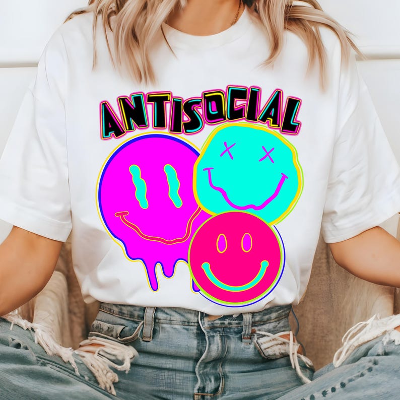 May include: White t-shirt featuring the word "ANTISOCIAL" in black, outlined in yellow and pink, above three smiley face graphics. The smiley faces are in pink, blue, and pink with black details.
